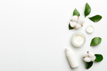Organic cosmetic products with cotton flower and green leaves on white background. Copy space, flat lay