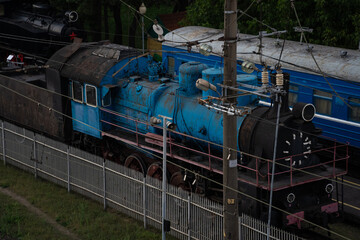 An old, blue, abandoned steam locomotive stands in a depot in the city