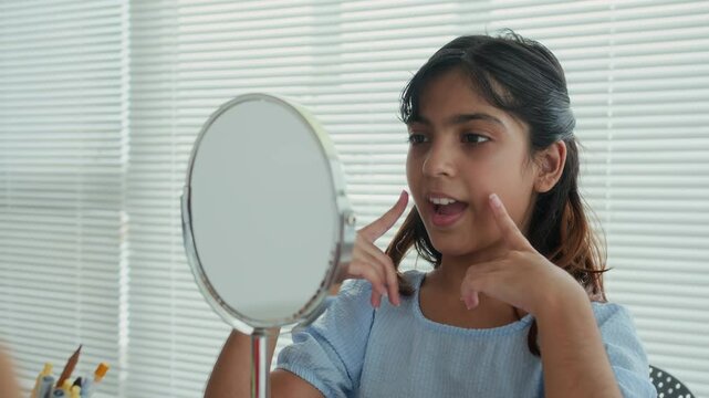 Medium close up of Indian schoolgirl training to pronounce sounds correctly using mirror during logopedic class
