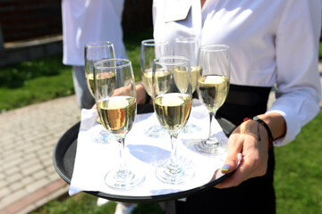 They are holding a tray with champagne glasses.