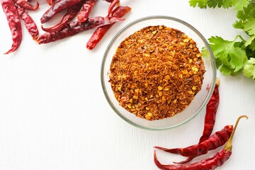 chilli powder in a glass cup with dried chilly on white background