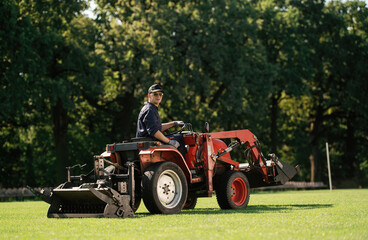 Sitting and driving. Man is with utility tractor with grass cutter and aerator equipment on the field