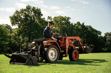 Obraz premium Man is with utility tractor with grass cutter and aerator equipment on the field