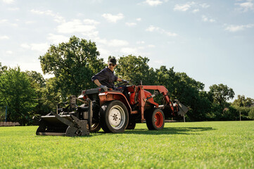 Loan work. Man is with utility tractor with grass cutter and aerator equipment on the field