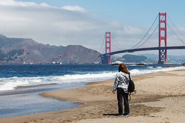 A person looks at the Golden Gate Bridge from a sandy beach