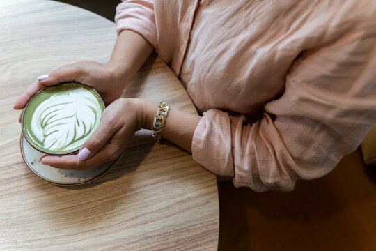 A woman holds a cup of matcha latte and latte art in her hands