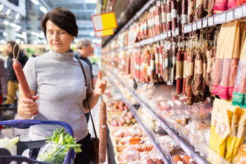 Older woman picking out sausage to buy in grocery store