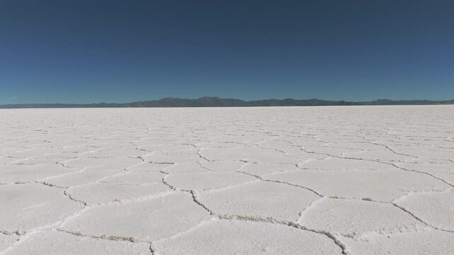 Aerial view from a drone advancing over the vast Salinas Grandes salt flats in Argentina, showcasing the expansive white surface and unique patterns of the salt lake.