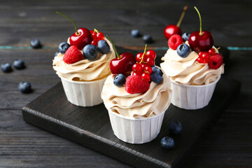 Tasty cupcakes with different berries on black wooden table, closeup
