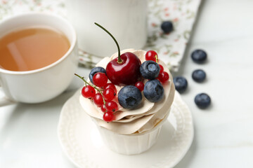Tasty cupcake with different berries and tea on white marble table, closeup