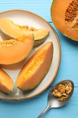 Cut ripe Cantaloupe melon and spoon with seeds on light blue wooden table, flat lay