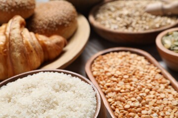 Different types of cereals, seeds, bread and legumes on wooden table, closeup