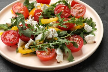 Tasty salad with arugula, cheese and vegetables on dark textured table, closeup