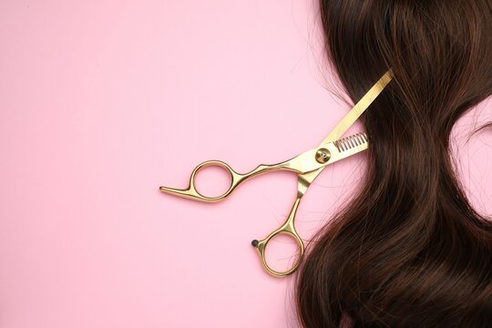 Brown hair strand and professional scissors on pink background, top view