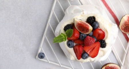 Pavlova cake (meringue dessert) with whipped cream, fresh berries, mint and fig on light grey table, top view