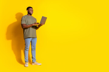 Photo of cheerful attractive man wear trendy clothes device wireless netbook empty space isolated on yellow color background