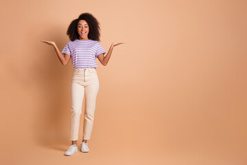 Full size photo of pretty young woman hold empty space vs wear t-shirt isolated on beige color background