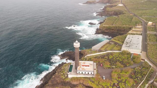 Aerial view of the scenic Faro de Punta Cumplida lighthouse amidst rocky cliffs and tranquil ocean waves with banana trees, Lomo Machin, La Palma, Canary Islands, Spain.