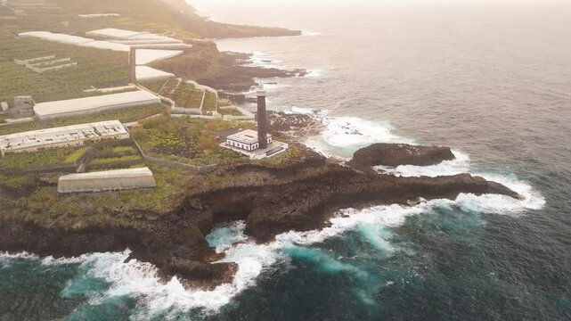 Aerial view of Faro de Punta Cumplida with banana trees and rocky shore at sunset, Lomo Machin, La Palma, Spain.