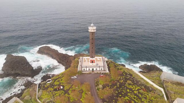 Aerial view of the serene Faro de Punta Cumplida lighthouse surrounded by rocky shore and banana trees, Lomo Machin, La Palma, Spain.