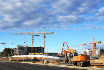 Construction site. Buildings under construction. Tower Cranes on Residential Buildings construction. Excavator on groundwork. Backhoe on roadworks. Excavator on earthworks for road construction.