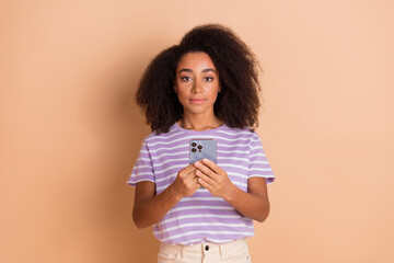 Portrait of pretty young girl hold phone wear striped t-shirt isolated on beige color background