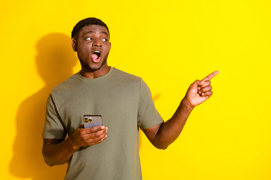 Photo of cheerful guy man wear khaki stylish clothes recommed empty space gadget isolated on yellow color background