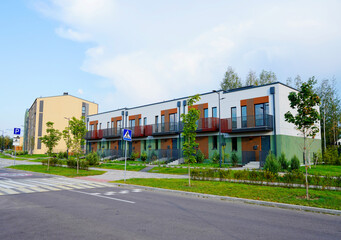 Fototapeta premium Townhouse facade exterior. Modern twin house design. Townhome in suburb. Modern complex of residential buildings. Two-storey house with Green lawn, trees, flowerbed, shrubs. Ecological green courtyard