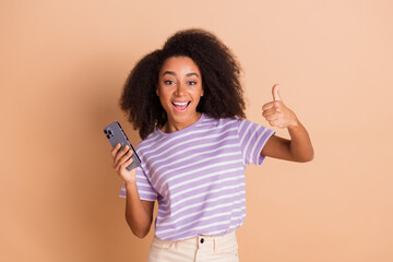 Photo of pretty young woman smart phone thumb up wear striped t-shirt isolated on beige color background