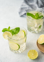 Two glasses lime cocktail with fresh citrus fruits on a light background. Summer refreshing mojito drink concept