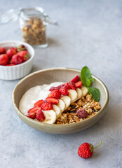 Natural greek yogurt with granola, strawberry and banana in a bowl on a blue background with fresh berries.
