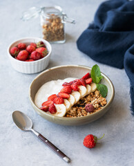 Natural greek yogurt with granola, strawberry and banana in a bowl on a blue background with fresh...