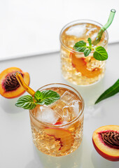 Homemade peach lemonade with ice and mint on white background. Fresh iced tea in glasses with light from the window close up.