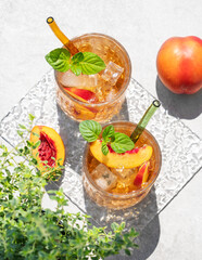 Peach lemonade with ice and mint on a concrete background. Fresh iced tea in glasses with shadow and herb.