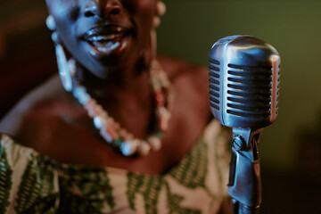 Selective focus closeup shot of young Black jazz vocalist singing song in microphone on stage