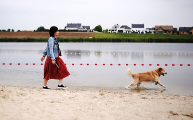 Playful Golden Retriever Runs And Plays With Its Female Owner On The Beach, Enjoying The Outdoors