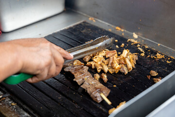 A person is cooking anticuchos on a grill