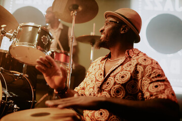 Cheerful Black man in hat playing conga in Afro-Cuban jazz band, medium closeup shot