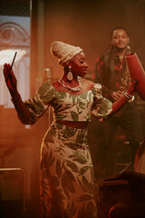 Vertical medium long shot of young Black woman wearing stylish clothes holding guiro giving jazz concert in local bar