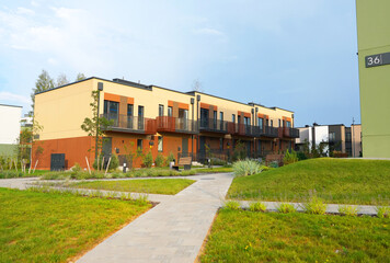 Sidewalk with green lawn at Modern Townhouse. Pedestrian path with flowerbed shrubs. Townhouse in suburb. Modern building in green enviroment. Street with Two-story townhouses in Gated Community. 