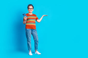 Full size photo of nice aged woman hold phone empty space wear t-shirt isolated on blue color background