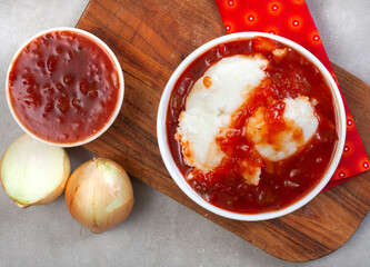 Traditional South African Pap and sauce, tomato and onion relish, flat lay with wooden board and ingredients on grey 