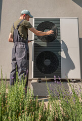 Technician adjusting an outdoor heat pump unit, surrounded by lush greenery at a residential...