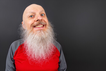 Elderly man with a long, white beard smiling widely against a dark background. His bright eyes and bald head emphasize his cheerful and friendly demeanor