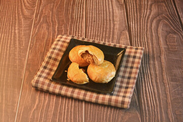 Chinese Pastry Mooncake baked round asian crispy cake with salted yellow red bean paste and eggs yolk in black plate on wood table Traditional halal menu food sweet dessert for autumn festival cafe