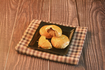 Chinese Pastry Mooncake baked round asian crispy cake with salted yellow red bean paste and eggs yolk in black plate on wood table Traditional halal menu food sweet dessert for autumn festival cafe