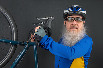 studio portrait of a cyclist in a helmet with a large white beard holding a bicycle in his hands on a dark gray background. sports and hobbies