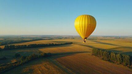 Obraz premium Aerial view of a bright yellow hot air balloon floating over a patchwork of fields, with a clear blue sky