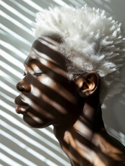 Handsome African guy with a shadow from a window frame on his face. Portrait of a man with white hair looking outside.