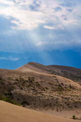 Sun rays breaking through clouds over desert dunes